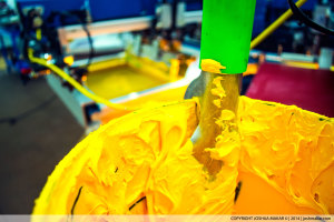 Photo of a bucket of bright yellow ink with a screen-printing press in the background.