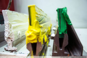 Photo of three screen-printing sqeegees with white, yellow, and green ink.